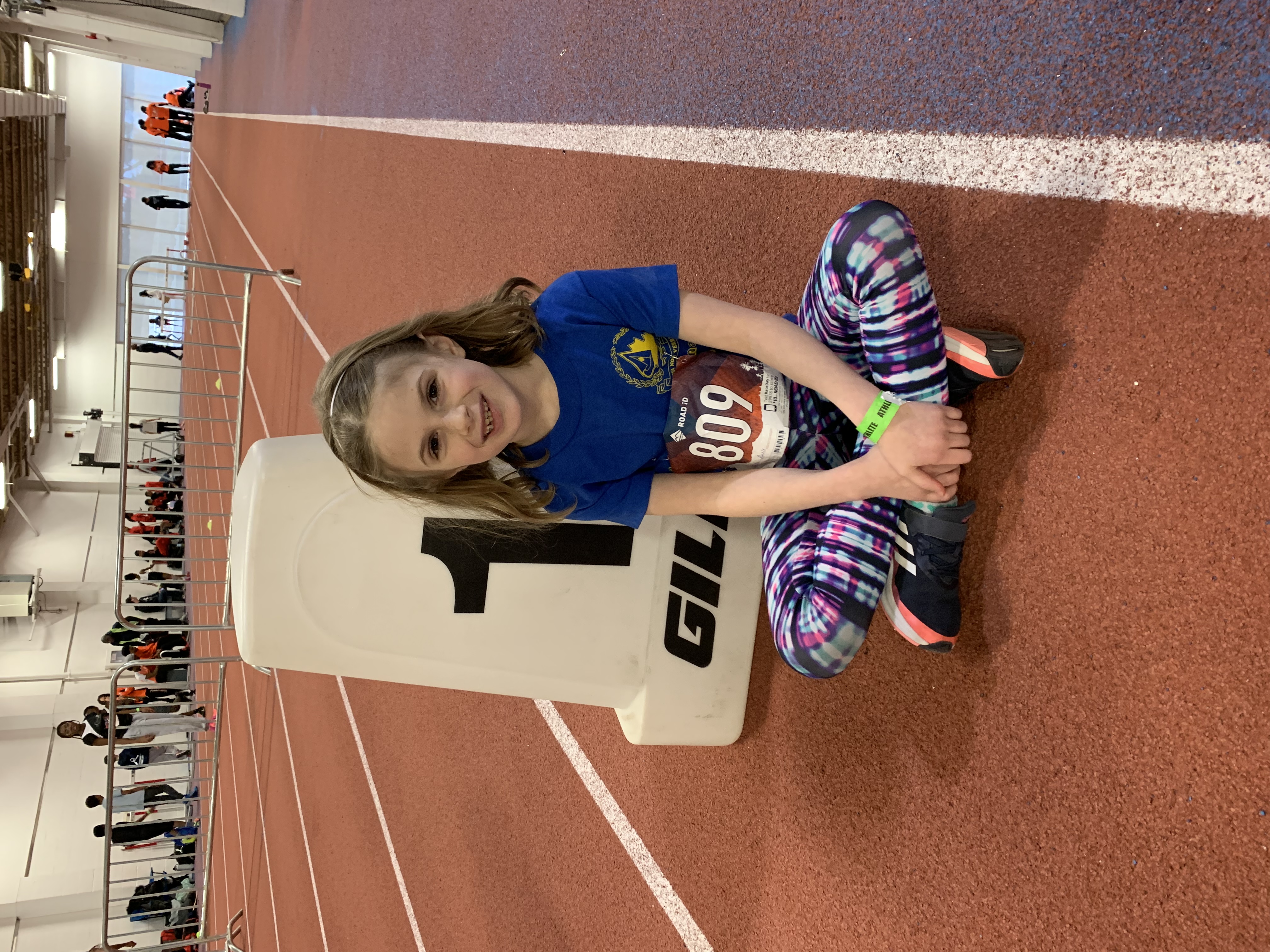Rosie White sits patiently beside her lane marker, waiting for the final of the Under-9 girls 60m, as part of the 2023 Ontario Indoor Track and Field Showcase at York University.  She was seventh in the Final, recording a Personal Record (P.R.) of 11.71 seconds. | Andrea Hammell